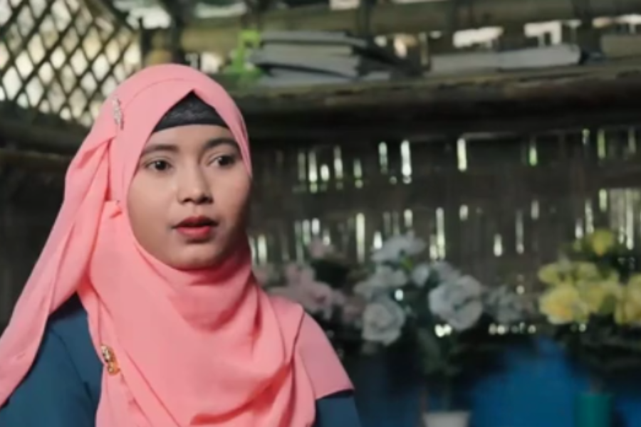 A woman who is a Rohingya refugee wearing a pink head scarf speaks to the camera.